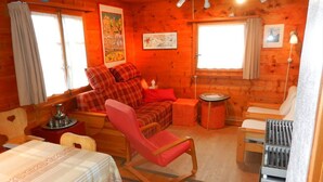 A cozy cabin interior with a wooden interior, a dining table, a sofa with red cushions, a rocking chair, and a small kitchenette. - Outdoor parking space - close to the cottage (at the start of the stairs) (St-Luc)