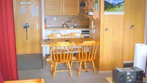 A compact kitchen with wooden cabinets, a microwave, and a sink. There are four wooden chairs around a small table. A refrigerator is visible in the corner. - Outside : Living on the 3rd floor of an apartment house, in Chandolin, for 2-4 persons, balcony with (Chandolin)