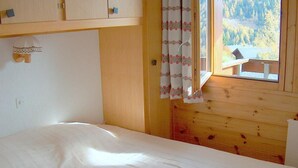 A bedroom with a bed, wooden walls, a window with a view of a cabin and forest, and a curtain with a floral pattern. - Outside : Living on the 3rd floor of an apartment house, in Chandolin, for 2-4 persons, balcony with (Chandolin)