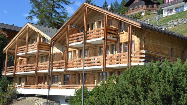 Een houten chalet met meerdere balkons, een stenen fundering en een bergachtige achtergrond.