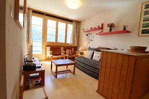 Een gezellige woonkamer met een houten bank, een klein tafeltje en een boekenkast.