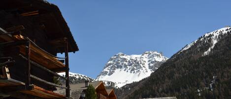 Un albergue de montaña con fachada de madera, un balcón y vistas a una montaña nevada.