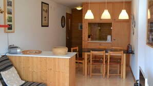 Een knus woongedeelte met een kitchenette, een houten eettafel en stoelen.