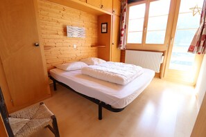 A bedroom with a wooden headboard, a bed with white bedding, a chair, and a window with curtains.