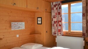 Een houten kamer met een bed, een ingelijst kunstwerk en een raam met gordijnen met een patroon.