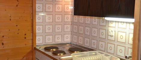 Uma cozinha com interior em madeira, fogão com três bocas, pia e painel de azulejos branco com padrão geométrico.