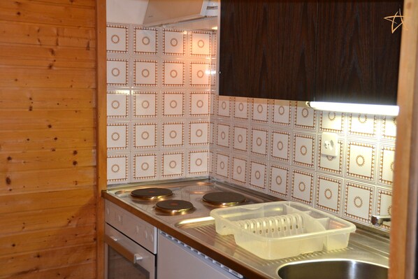 A kitchen with a wooden interior, a stove with three burners, a sink, and a white tiled backsplash with a geometric pattern.
