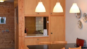 Een houten keuken met een eettafel en stoelen, hanglampen en een rode broodrooster.