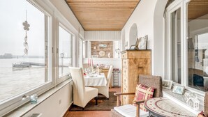 Habitación con vista a un puente sobre el agua, zona de comedor con mesa para dos, y un armario de madera con objetos decorativos.