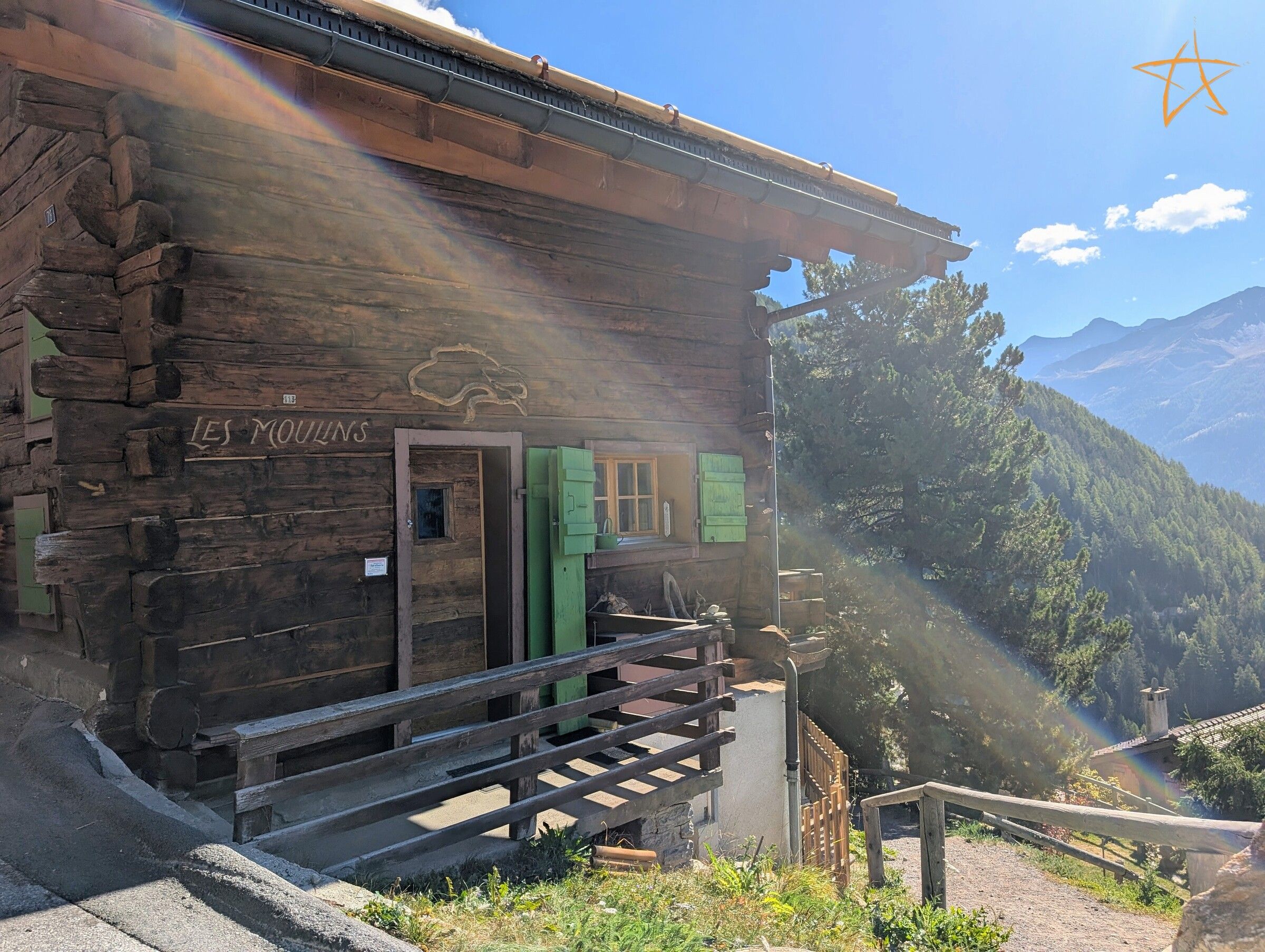 Ein rustikales Holzgebäude mit einem Schild, auf dem 'LES MOUJINS' steht, und einer Holztreppe, die zu einer Tür führt.