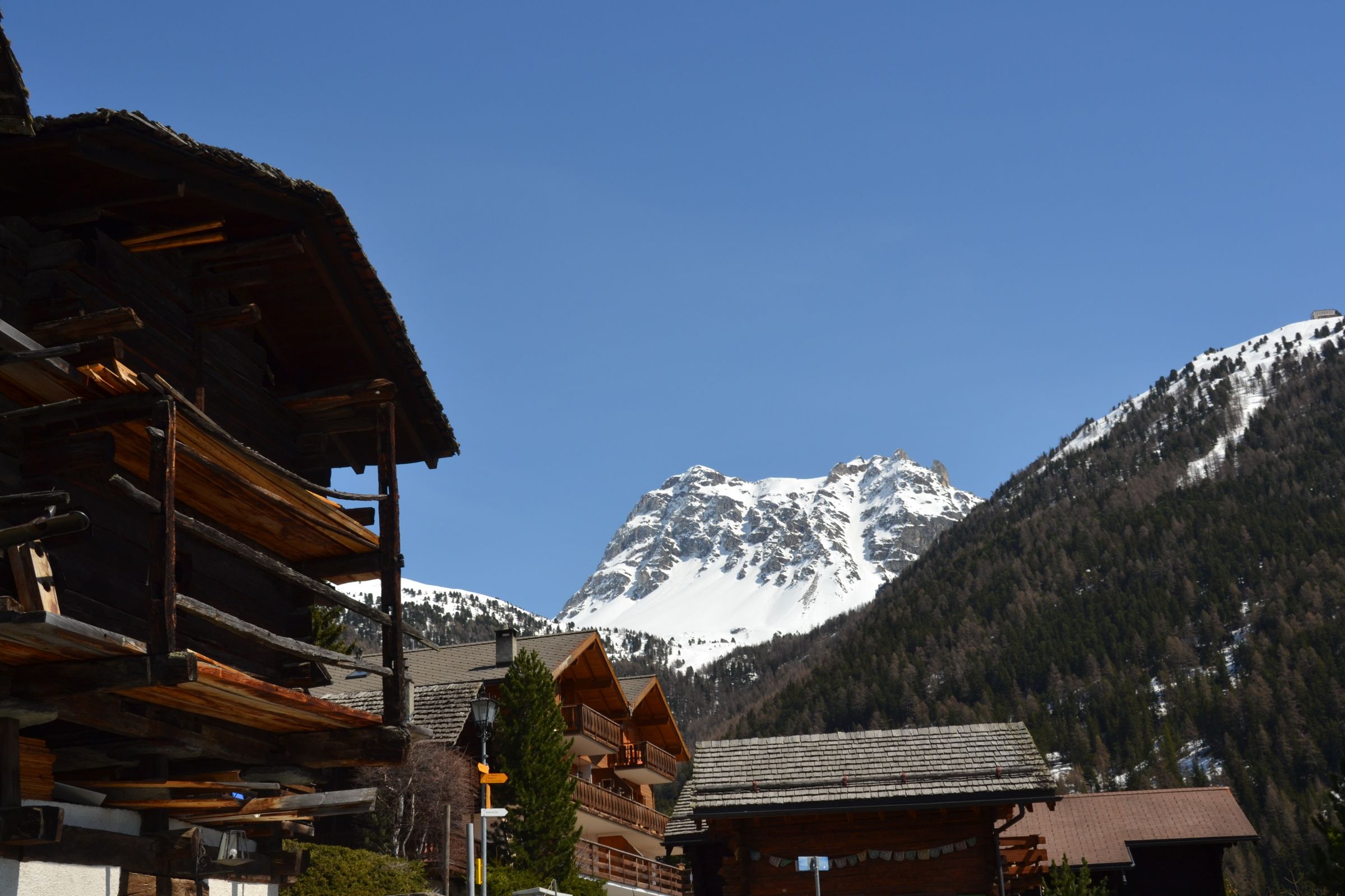 Un chalet de montagne avec une façade en bois, un balcon et une vue sur une montagne enneigée.