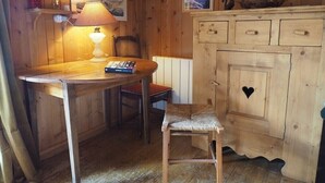 Ein Holzblockhaus-Interieur mit Esstisch, Stuhl, Lampe, einer Kommode mit Schubladen und einem gerahmten Bild an der Wand.