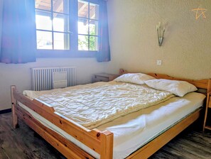 Un dormitorio con cama de madera, un radiador, una mesita de noche y una ventana con cortinas.