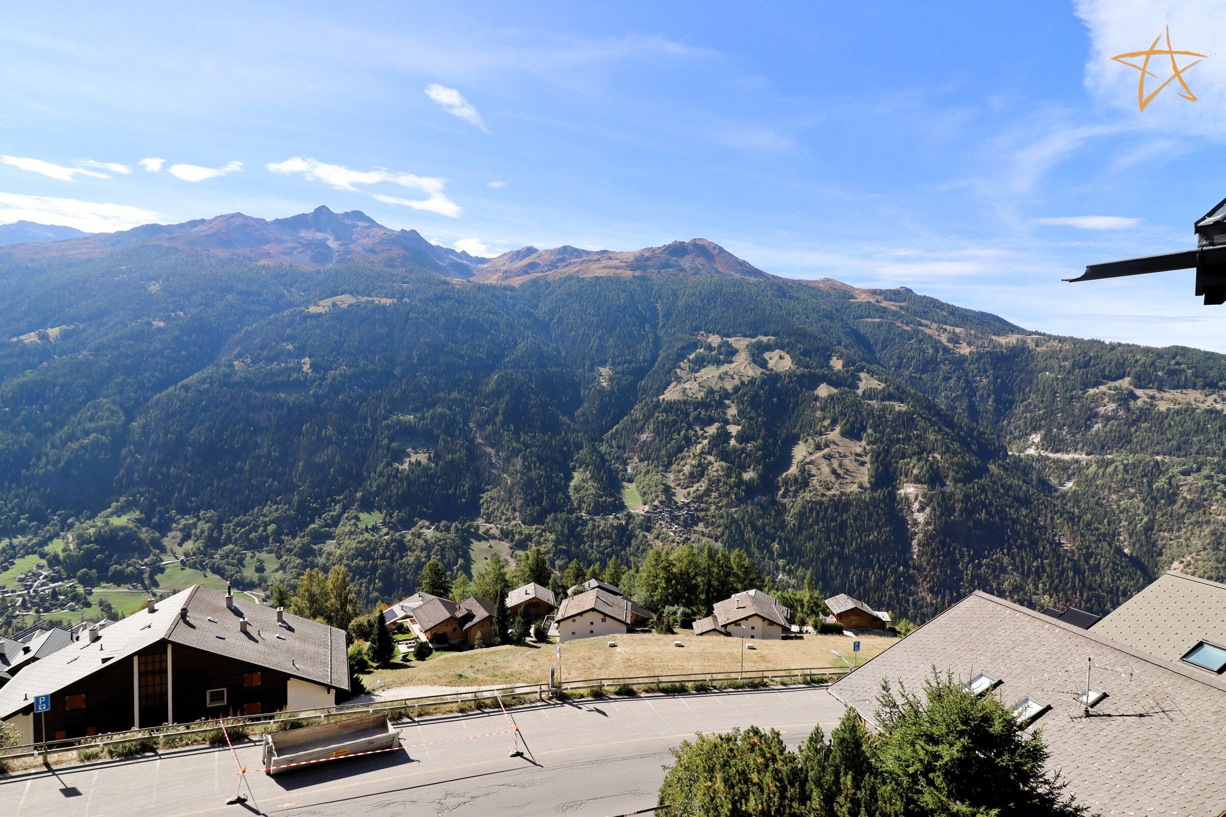 Un paisaje montañoso con un pueblo, casas con techos inclinados y un camino pavimentado.