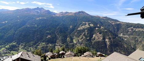 Un paisaje montañoso con un pueblo, casas con techos inclinados y un camino pavimentado.