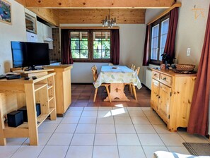 Una cocina compacta con comedor, muebles de madera, un televisor y una ventana con cortinas.