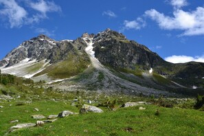A mountain landscape with a clear sky, rocky terrain, and a small herd of sheep.