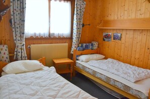 A wooden cabin room with two single beds, a small wooden table, and a radiator.