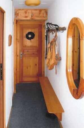 Ein schmaler Flur mit einer Holzbank, einer Tür mit rundem Fenster und einem Garderobenschrank mit einem aufgehängten Mantel.