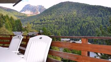 Une terrasse en bois avec des chaises blanches donnant sur une montagne boisée.