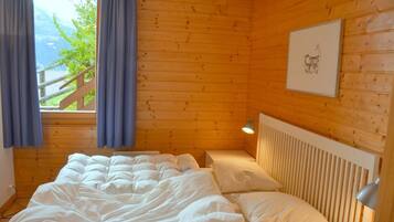 Ein Zimmer in einer Holzhütte mit einem Bett, einem Nachttisch, einer Lampe und einem Fenster mit Vorhängen.