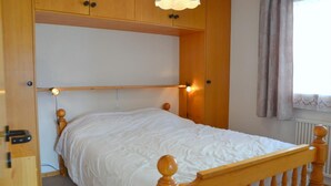 En säng för en person med en sänggavel och en fotgavel i trä, ett vitt överkast och två sänglampor.