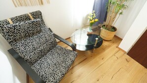 A corner room with a patterned sofa, a small glass table with a vase, and a bamboo plant. - Apartment No. 03 in Vienna near Schönbrunn/Westbahnhof | Keyless Check-In (Rudolfsheim-Fünfhaus)