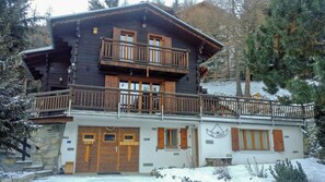 Eine zweistöckige Holzhütte mit Balkon, Steinfundament und einem Schild mit der Aufschrift 'La Voliere'.