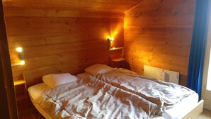 A cozy wooden cabin room with a bed, a chair, and a nightstand with a lamp. - Chalet VOLIÈRE HAUT -Outside : chalet for 8 persons, large terrace, garden, balcony, barbecue, sun t (St-Luc)