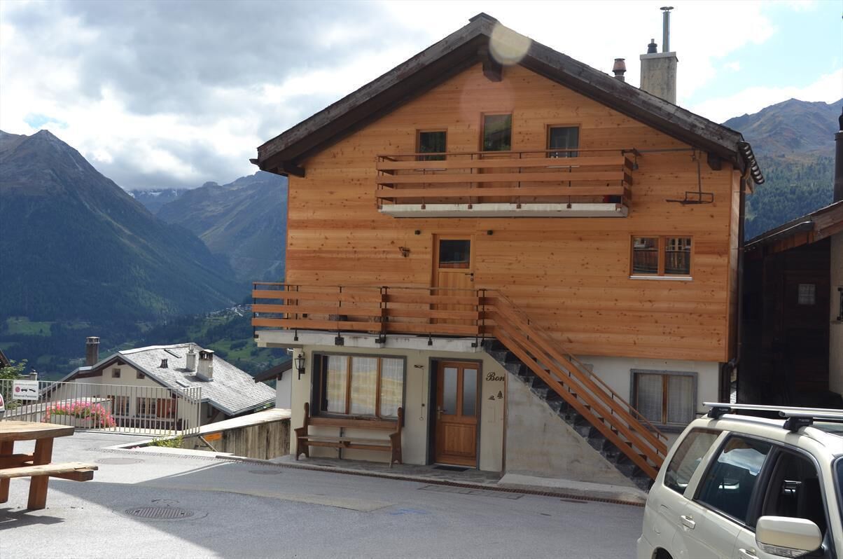 A wooden chalet with a balcony, a staircase, and a view of mountains.