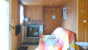 Un accogliente interno di una baita con camino in pietra, pareti in legno e un letto con una coperta patchwork colorata.