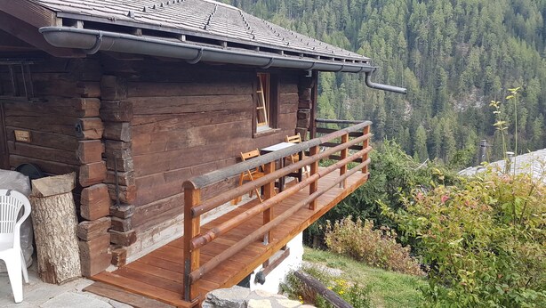 Una baita di legno con un balcone, pareti in legno massiccio e vista su una montagna boscosa.