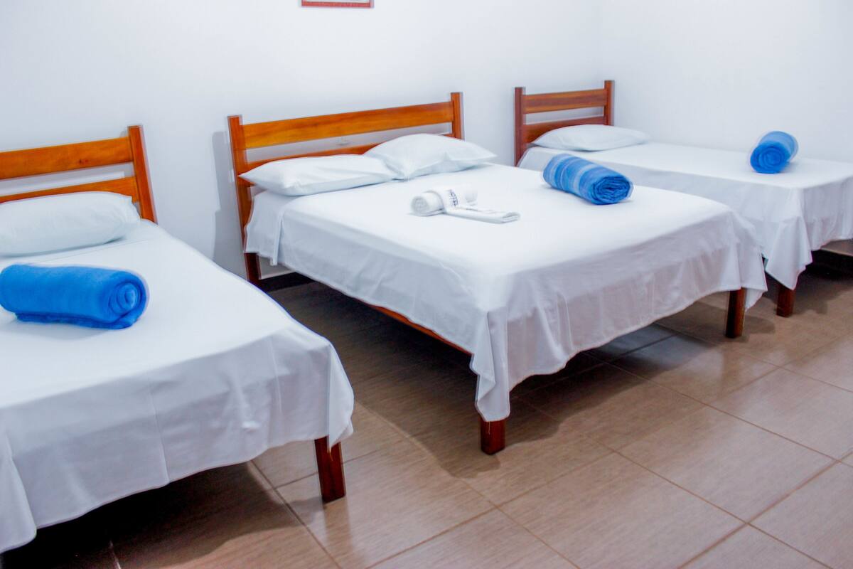 A hotel room with three single beds, each with a wooden headboard and white bedding.