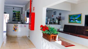 Un espace d’accueil d’hôtel comprenant un comptoir de réception, un bac à fleurs en bois orné de fleurs rouges, un canapé marron et un tableau accroché au mur.