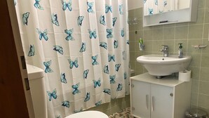 A bathroom with a toilet, sink, and shower curtain. - Outside: 3-room apartment for 5 people on the lower floor, balcony -Interior: 90 m2, closed entrance (St-Luc)