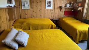 A room with two beds covered in yellow bedding, wooden panel walls, and framed artwork. - Outside: 3-room apartment for 5 people on the lower floor, balcony -Interior: 90 m2, closed entrance (St-Luc)