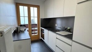 A kitchen with white cabinets, a black countertop, and a window with a view. - Outside: 3-room apartment for 5 people on the lower floor, balcony -Interior: 90 m2, closed entrance (St-Luc)