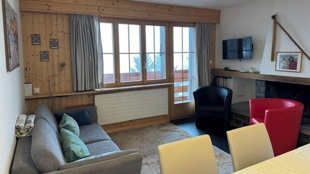 A cozy living room with a sofa, chairs, a dining table, a fireplace, and a TV. - Outside: 3-room apartment for 5 people on the lower floor, balcony -Interior: 90 m2, closed entrance (St-Luc)