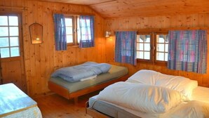 A wooden cabin room with two beds, a small table, and a window with curtains.