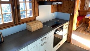 A compact kitchen with wooden walls, a built-in stove, and a window with blinds.