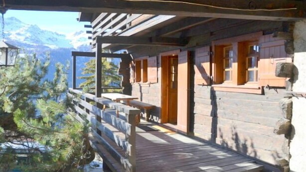 A wooden cabin with a wooden deck and a view of mountains.