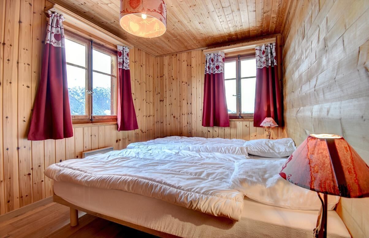 A wooden cabin bedroom with two beds, large windows, and a hanging light fixture.