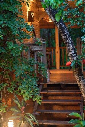 A wooden staircase leading to a cabin labeled "Cabane," surrounded by lush greenery. - Family fun... The star cabin (Deshaies)