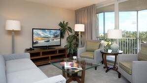 Ein Hotelzimmer mit Flachbildfernseher, zwei Sesseln, einer Couch, einem Glastisch und einem Balkon mit Blick.