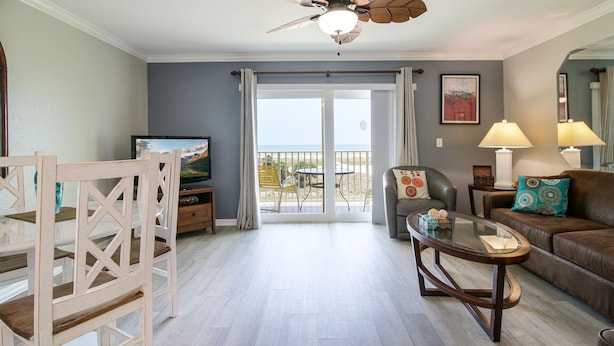 Una sala de estar con televisor, sofá, mesa de centro y balcón con vista a la playa.