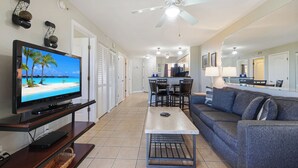 A living room with a TV, a sofa, a coffee table, and a dining area with chairs and a table. - Surf Beach 305 - Spectacular Sunsets - Beach Front (Treasure Island)