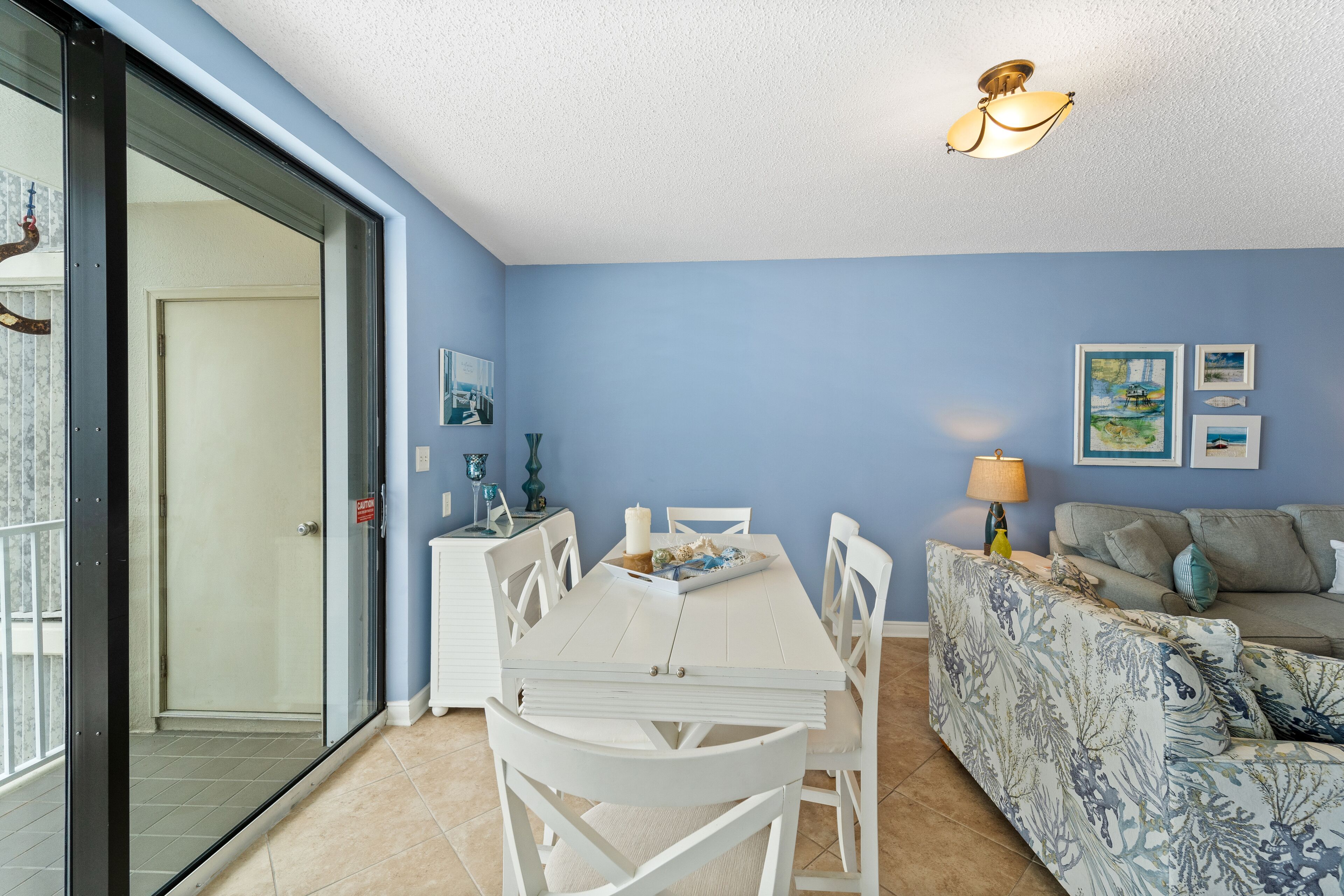 A dining area with a white table and chairs, a patterned sofa, and a ceiling light fixture.