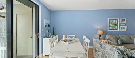 A dining area with a white table and chairs, a patterned sofa, and a ceiling light fixture.