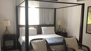 Ein Bett mit Baldachin, zwei Nachttische, zwei Korbstühle und ein Deckenventilator.