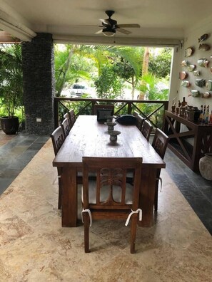 A wooden dining table with chairs, a ceiling fan, and a view of greenery outside.